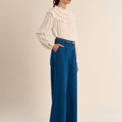 Mulher com camisa creme folhos e calças largas de ganga azul escuro