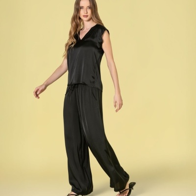 Conjunto feminino de pijama preto acetinado com blusa e calças largas, com sandálias pretas em fundo amarelo.