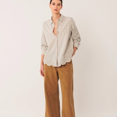 Mulher a usar camisa bege clara bordada e calças largas castanhas