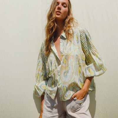 Mulher com camisa padrão abstrato verde e amarelo e calções cinza claro