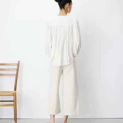 Mulher de costas com blusa branca, calças largas brancas e sapatos rasos creme