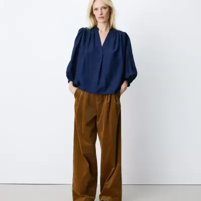 Mulher com blusa azul escuro e calças largas camel em fundo branco