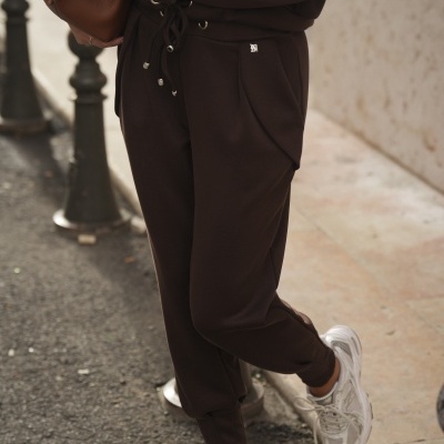 Calças e sweatshirt castanhas com cordão e sapatilhas brancas num cenário urbano.