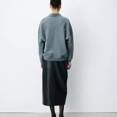 Pessoa de costas com camisola cinza e saia preta de couro