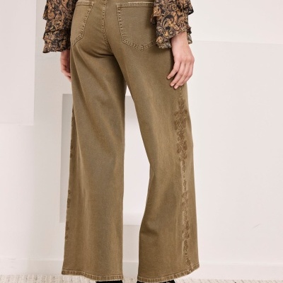 Calças largas castanhas de ganga com botins pretos e camisa estampada visível de costas