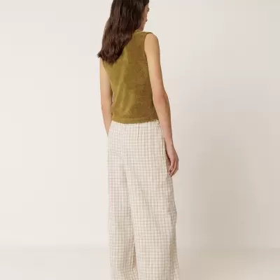 Mulher vista de costas com top verde musgo sem mangas e calças largas xadrez bege e branco