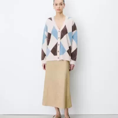 Mulher com cardigan colorido, saia bege e sapatos baixos bege, fundo branco.
