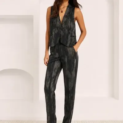 Fato feminino preto com padrões cinzentos e detalhes dourados, colete e calças, sandálias pretas de salto grosso.