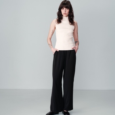 Pessoa vestindo camisola branca de gola alta sem mangas e calças pretas largas num fundo cinza