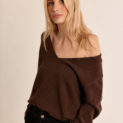 Mulher de cabelos loiros com camisola castanha de malha e calças pretas
