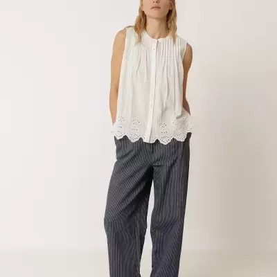 Mulher com blusa branca sem mangas e calças largas riscas finas azuis e brancas