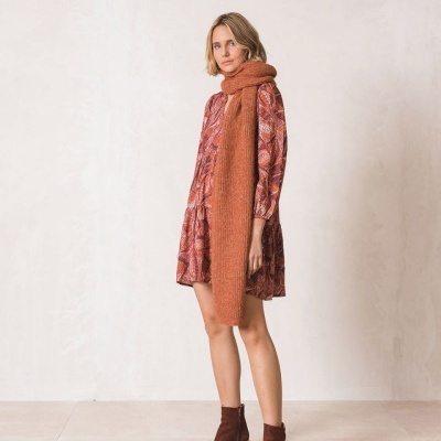 Mulher usando vestido vermelho com padrão, cachecol laranja e botins castanhos