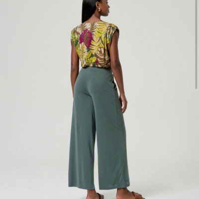 Mulher com calças largas verdes e blusa estampada de folhas coloridas