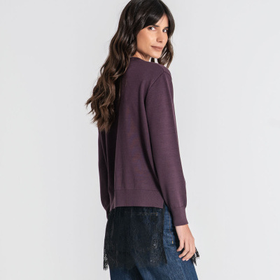 Mulher de perfil veste sweater roxo e calças de ganga com detalhe em renda preta.