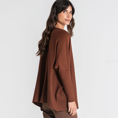 Mulher com camisola castanha de malha e calças castanhas em fundo branco