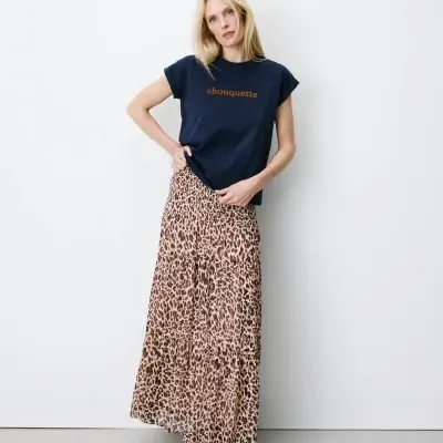 Mulher veste t-shirt azul escura com texto e saia plissada padrão animal print.