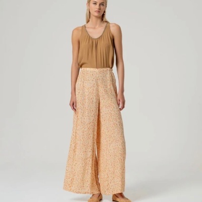 Mulher com top castanho, calças largas creme com padrão laranja e sapatos castanhos trançados