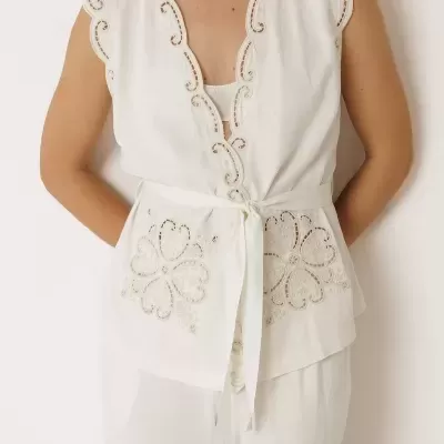 Blusa branca sem mangas com bordados florais e faixa na cintura, combinada com calças brancas.