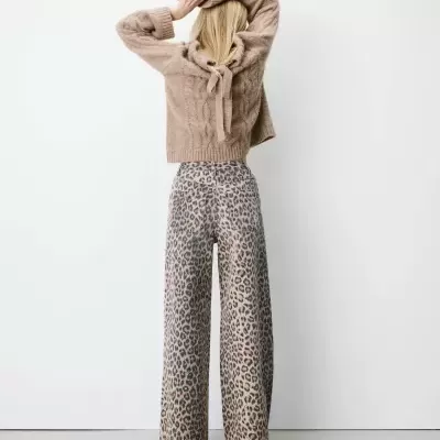 Mulher de costas com camisola castanha trançada e calças leopardo