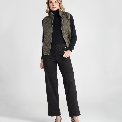 Mulher com colete verde-oliva acolchoado, camisola preta, calças pretas e sapatos de salto preto