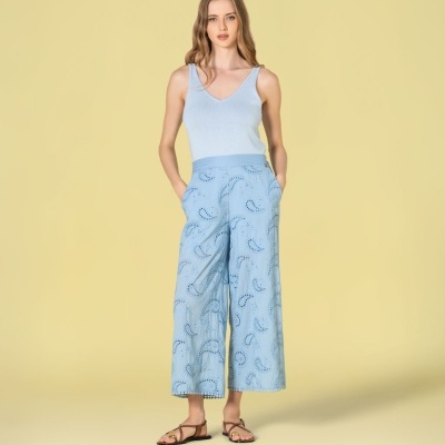 Mulher com top azul claro e calças culotte azul claro com recortes e sandálias marrons.