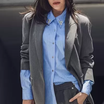 Conjunto de blazer e calças cinzentas com camisa azul de riscas brancas e mala bege