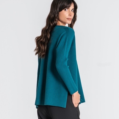 Mulher de camisola azul-petróleo e calças pretas em fundo branco