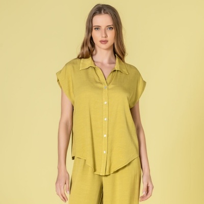 Mulher a usar conjunto amarelo mostarda composto por camisa de botões e calças largas em fundo amarelo claro