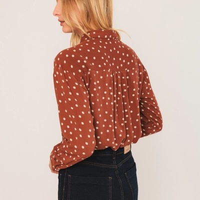 Blusa castanha com bolinhas brancas vista de trás, usada com calças de ganga escuras.