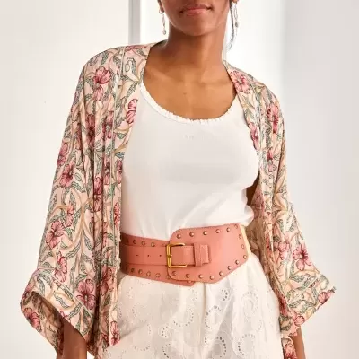 Mulher com camisola branca, calças de renda brancas, cinto rosa largo e casaco floral