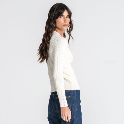 Mulher de cabelo castanho vestindo camisola branca de malha e jeans azul.