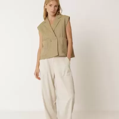 Mulher com colete sem mangas bege às riscas e calças largas creme com mocassins bege