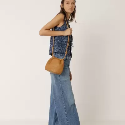 Mulher com blusa azul, calças de ganga largas, sandálias pretas e bolsa castanha em fundo branco