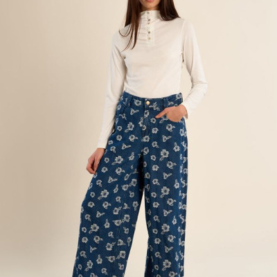 Mulher com body branco e calças largas de ganga azul com flores brancas