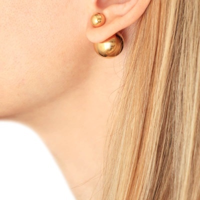 Brincos dourados de esfera em orelha com cabelo loiro