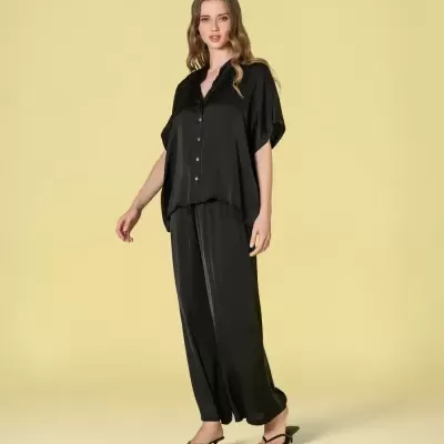 Conjunto pijama acetinado preto com camisa e calças largas e sandálias pretas.