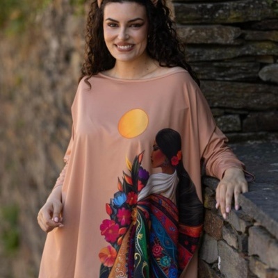 Blusa bege com estampa colorida de mulher e flores, usada por mulher junto a parede pedra