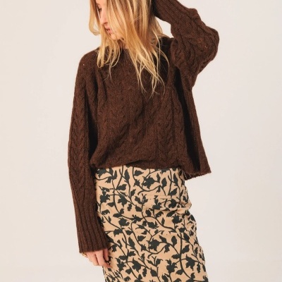 Mulher a usar camisola castanha de malha e saia bege com padrão floral preto