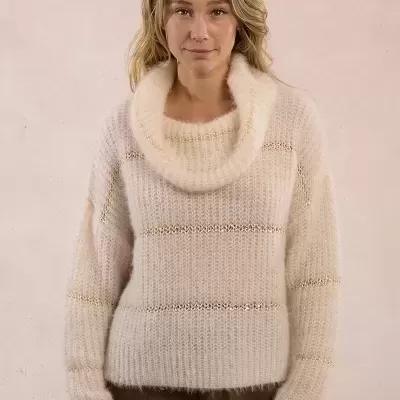 Mulher a usar camisola de malha creme com riscas douradas e calças castanhas.