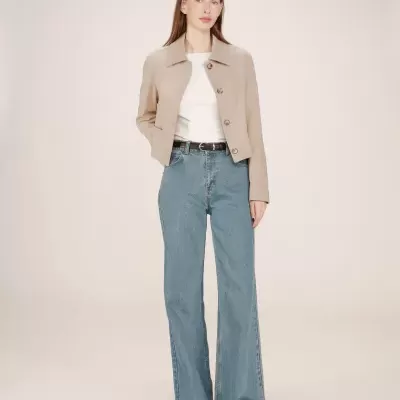 Mulher a usar casaco bege, t-shirt branca e calças de ganga largas azuis