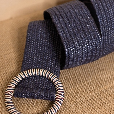 Cinto azul escuro trançado com fivela redonda colorida sobre tecido de juta.