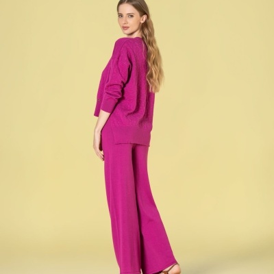 Mulher com conjunto rosa de camisola e calças largas com sandálias castanhas, fundo amarelo claro