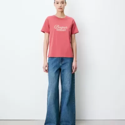 T-shirt rosa com texto branco e jeans largos azuis em fundo branco
