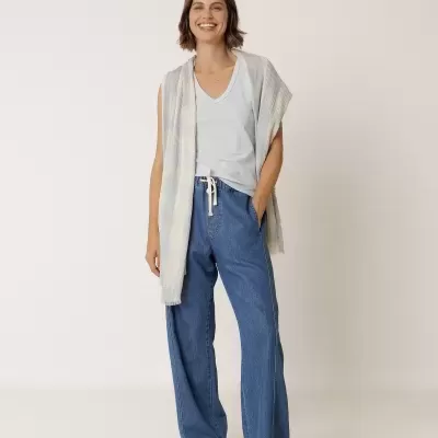 Mulher com camisola branca, calças de ganga largas e camisola leve às riscas pastel