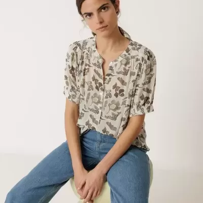 Mulher com blusa floral e calças de ganga sentada em esfera creme