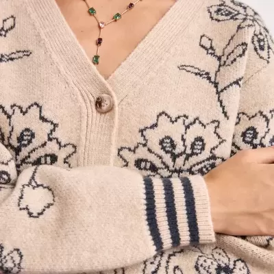 Casaco bege de malha com padrão floral preto e detalhes nas mangas, usado com colar colorido.