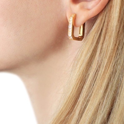 Brinco argola quadrada dourada usado na orelha de mulher loira