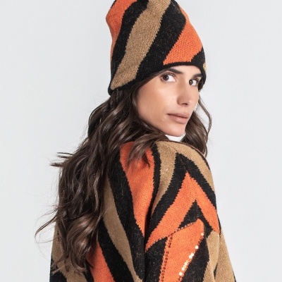Mulher com gorro e suéter de malha laranja, preto e bege com padrão geométrico