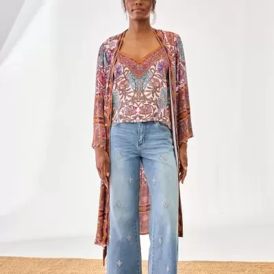 Mulher com roupa de padrão floral e calças de ganga bordadas em ambiente claro