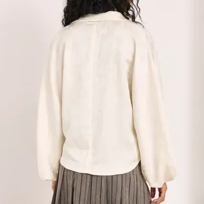 Blusa creme com padrão jacquard e saia plissada cinza vista de costas